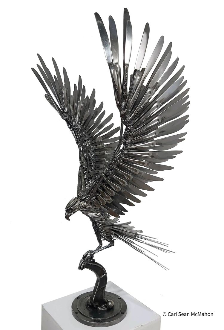 Free-standing metal hawk sculpture with wings raised, front-left view on abstract metal base.