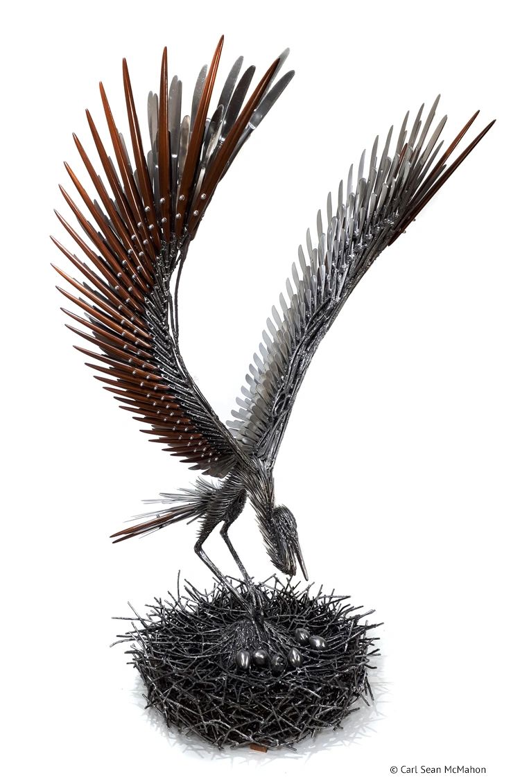 Front-right angle of heron sculpture standing in metal nest with eggs and dark cedar featherwork.