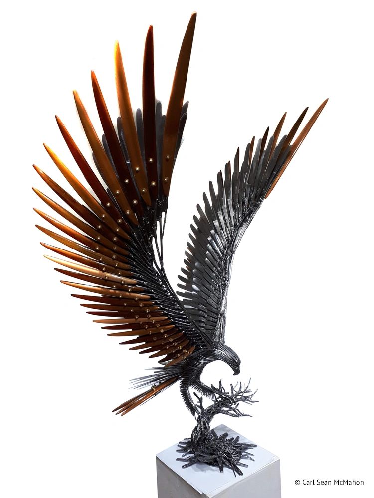 Reclaimed metal eagle with cedar wings perched on tree base, feet grounded in landing position