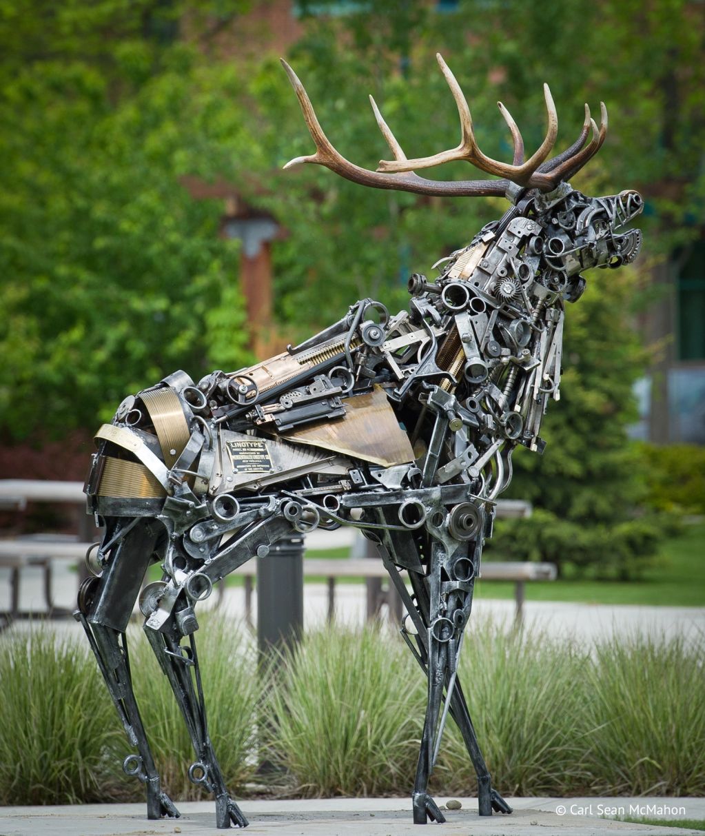 Metal sculpture of a deer with realistic antlers in a park.