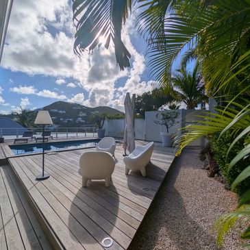Sunny outdoor deck with modern chairs and pool under blue sky.