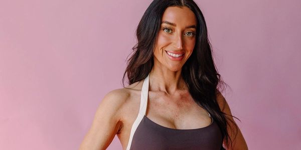 Smiling woman with long dark hair posing against a pink background.