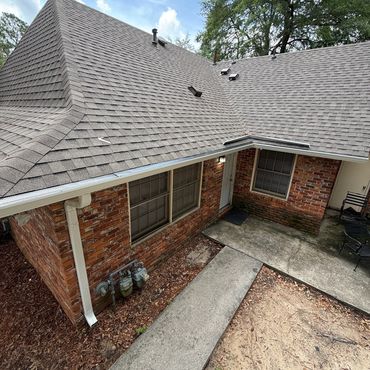 A brick house with a gray shingled roof and concrete walkway on a sunny day.
