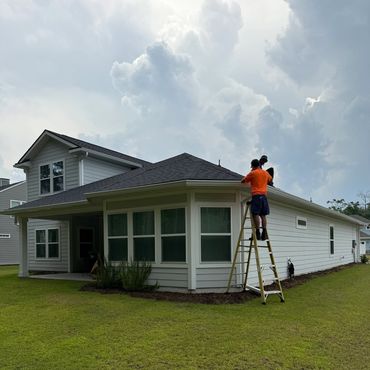 Two men working on a house roof with a ladder on a cloudy day.