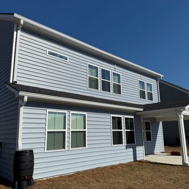 A two-story house with light blue siding and multiple windows under a clear blue sky.