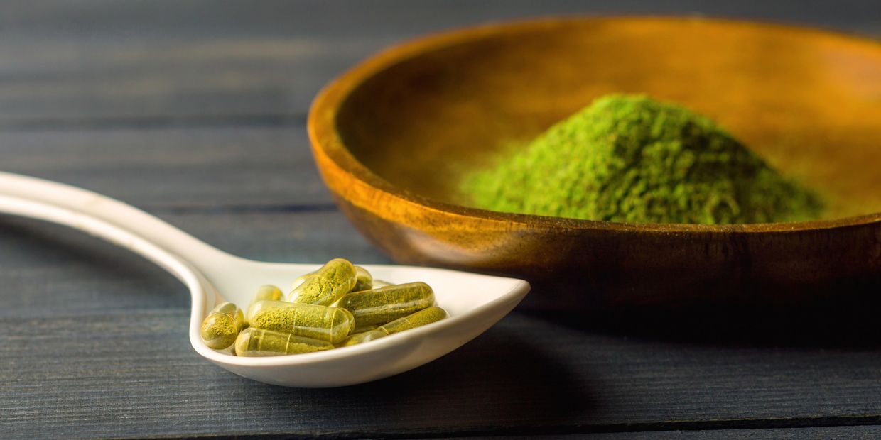 green maeng da kratom powder in a bowl with kratom capsules in a spoon on a table