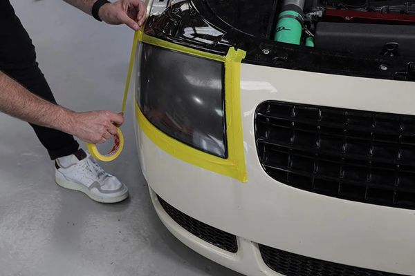 A guys using yellow tape to mask off a headlight for a headlight restoration auto detailing service