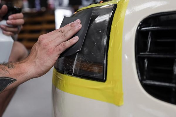 A guy using his hand to wet sand an Audi headlight during a headlight restoration detailing service 