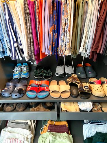 Neatly organized closet with folded clothes, hanging pants, and arranged shoes.A well-organized closet featuring folded garments, hanging trousers, and systematically arranged footwear.