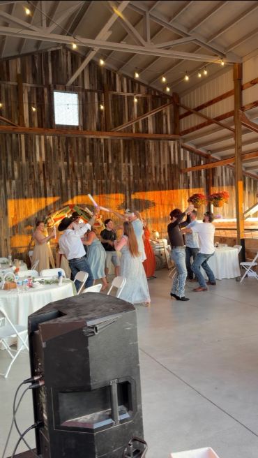 People dancing joyfully in a barn decorated with string lights.