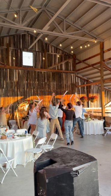 People dancing in a rustic indoor event space with string lights.