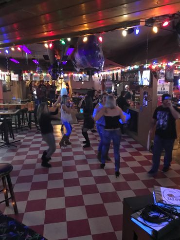 People dancing in a dimly lit bar with colorful lights.