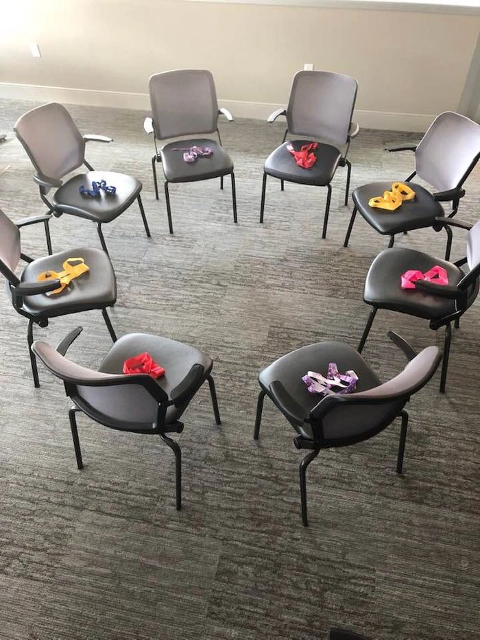 A group of gray chairs arranged in a circle with a colorful ribbon laid on each seat.