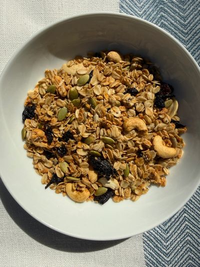 A bowl of granola with nuts and dried berries on a tablecloth.