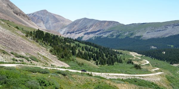 Winding mountain road with green hills and clear blue sky.