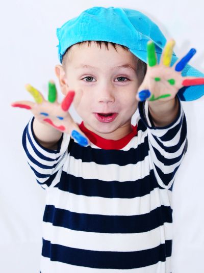 Child with colorful painted hands and blue cap.