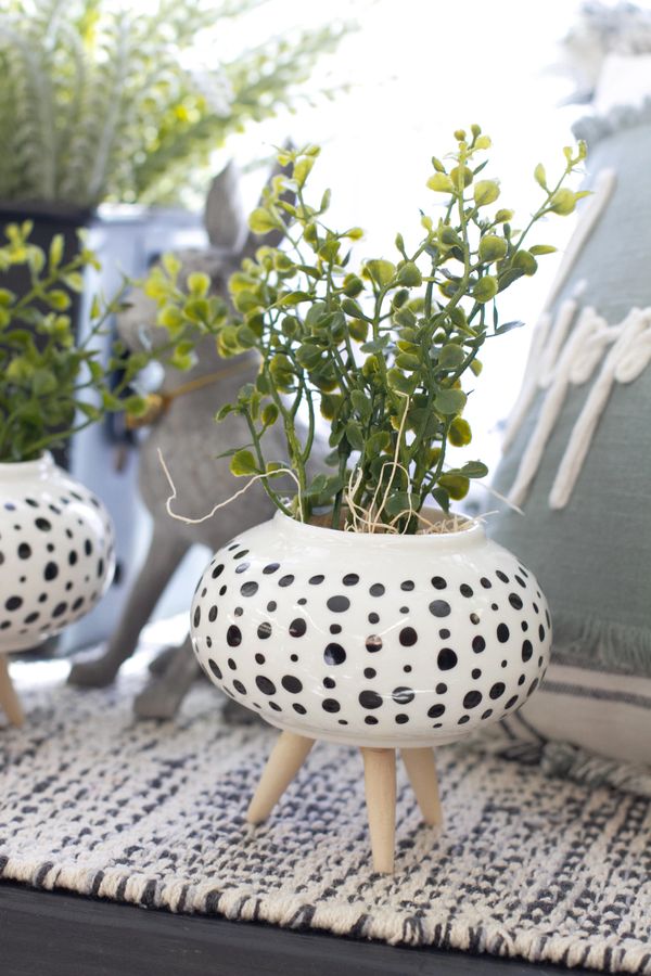 Realistic artificial plant in a white/dotted ceramic plant holder with wooden tri-legs