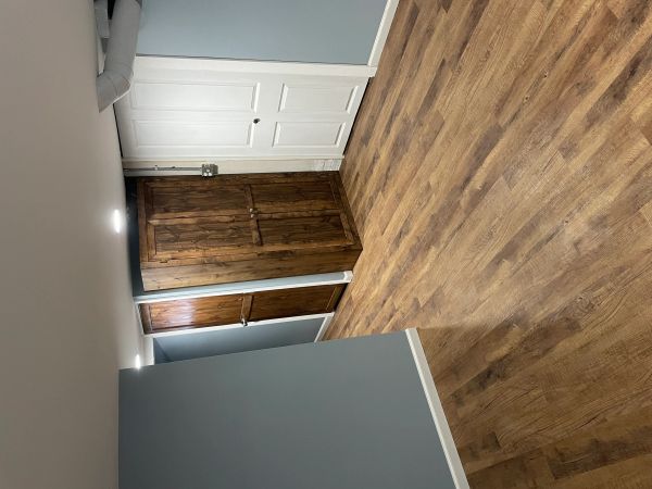 Basement hallway with wooden and white doors, gray walls, and wood flooring.
