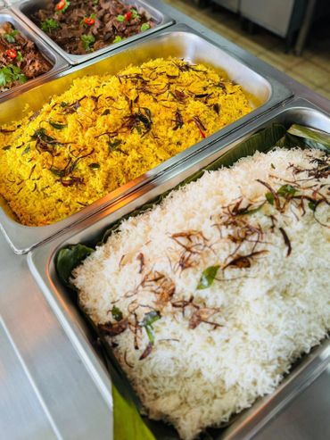 Buffet trays with yellow and white rice garnished with herbs and spices.