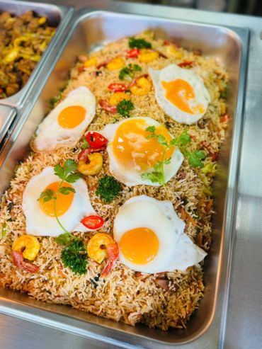 Tray of fried rice topped with sunny-side-up eggs and garnished with herbs and chili slices.