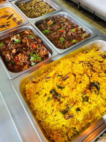A vibrant buffet with yellow rice and various meat dishes garnished with herbs and chili.