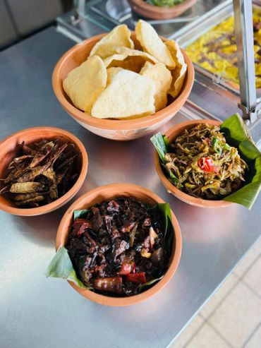 Assorted traditional dishes served in clay bowls with crispy chips on a metal table.