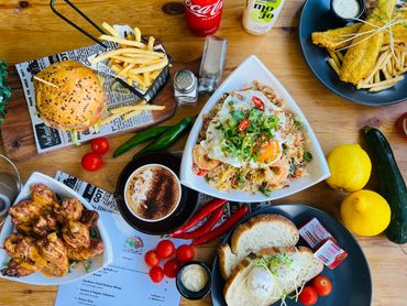 A colorful spread of diverse dishes including a burger, fries, rice with egg, chicken wings, and drinks on a wooden table.