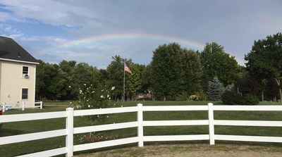 a rainbow in the sky arcing over an American flag in front of a barn