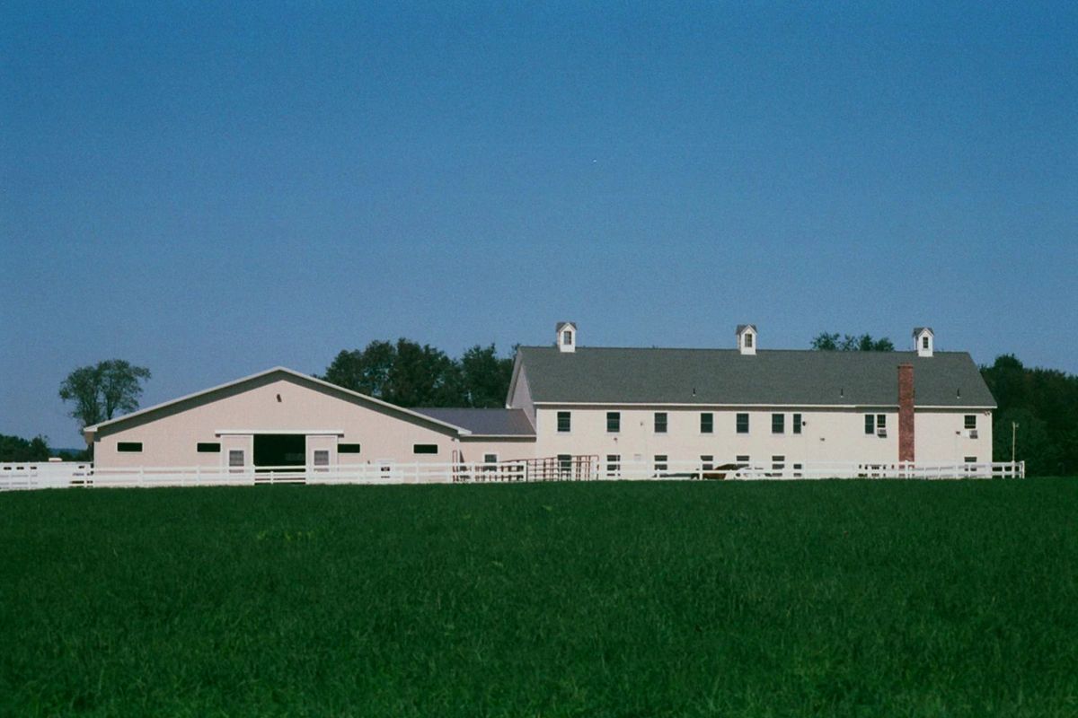 view of the side of the barn and an outdoor arena surrounded by white fencing