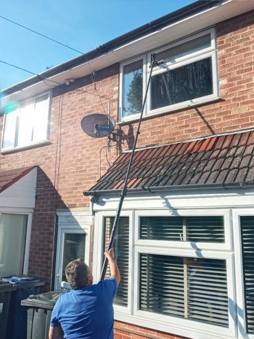 Window cleaner using water-fed pole to clean upper windows in Greenford home.