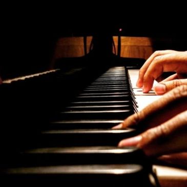 Hands playing piano keys in a dimly lit room.
