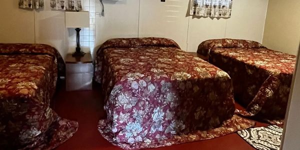 Room with three beds covered in floral bedspreads and a small nightstand with a lamp.