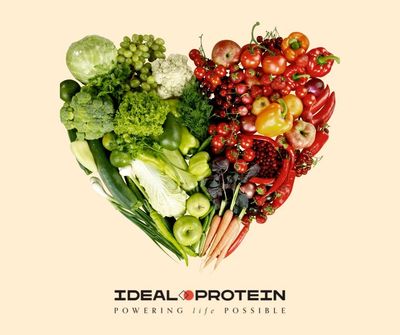 Heart-shaped arrangement of fresh green and red fruits and vegetables with Ideal Protein logo.