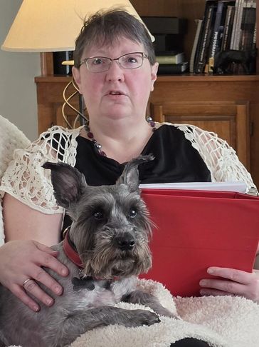 Woman reading a book with a dog on her lap in a cozy room.