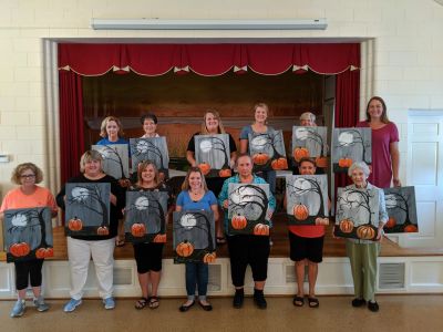 Group of women holding Halloween-themed paintings with pumpkins.