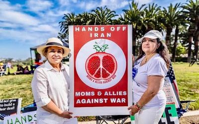 Two women holding a protest sign against war with Iran.