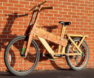 A bicycle made primarily of wood against a brick wall.