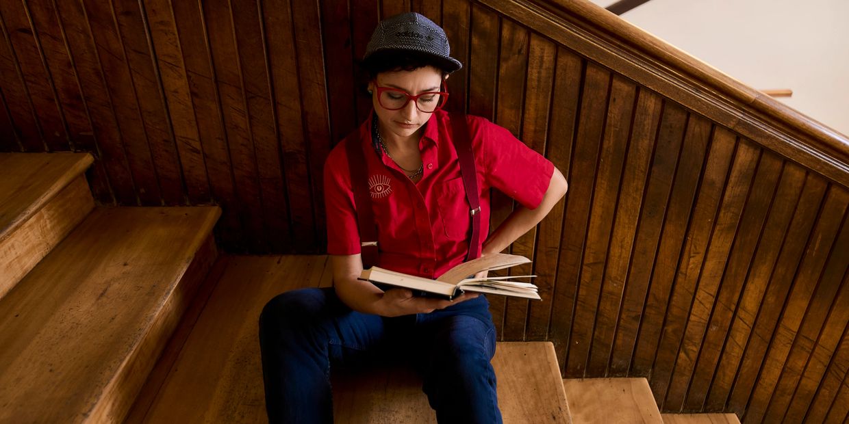 Person in red shirt and cap reading a book on wooden stairs.
