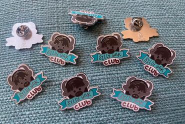 Multiple enamel pins with a cartoon yak and 'Silly Yak Club' text on a textured surface.