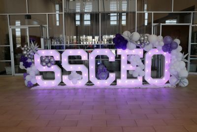 Illuminated balloon decorations spelling "CSCD" in purple and white.