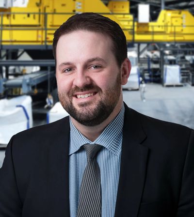 A man in a suit and tie smiles in an industrial setting.