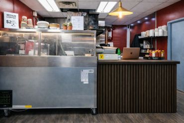 Coffee shop counter with a laptop and condiment bottles.