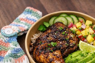 Grilled chicken leg with rice, avocado, cucumber, and salsa in a bowl.