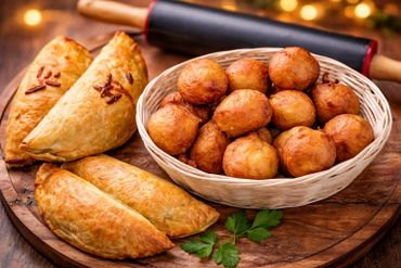Basket of golden fried dough balls with baked turnovers on a wooden board.