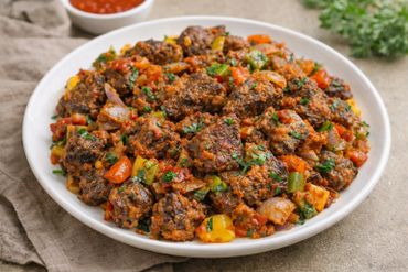 Plate of spicy, cooked vegetables and meat pieces garnished with herbs.