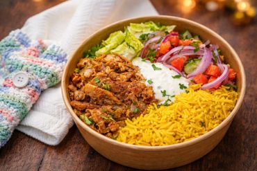 A colorful bowl with grilled meat, yellow rice, salad, and yogurt sauce.