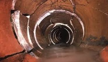 Inside view of a rusty, circular tunnel with water flowing through.