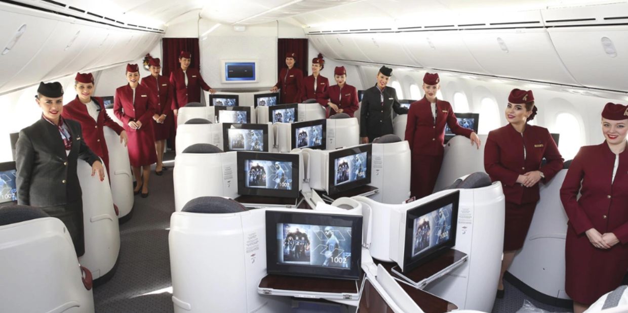 Flight attendants pose inside a luxurious airplane cabin with spacious seats and personal screens.