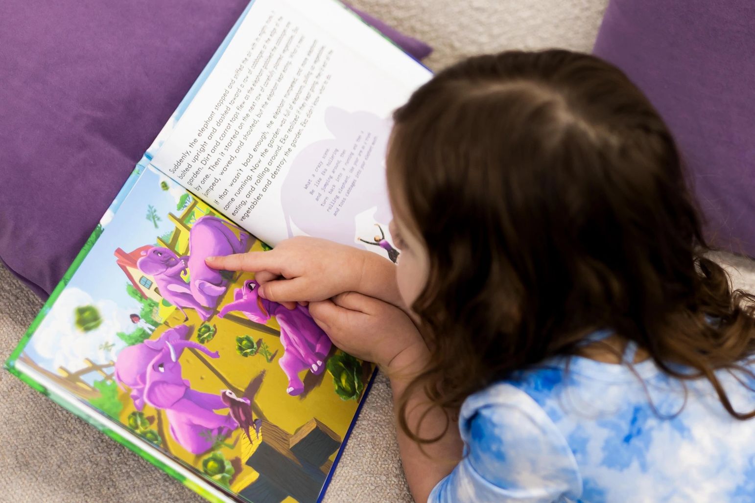 little girls looking at a page of the book with purple elephants