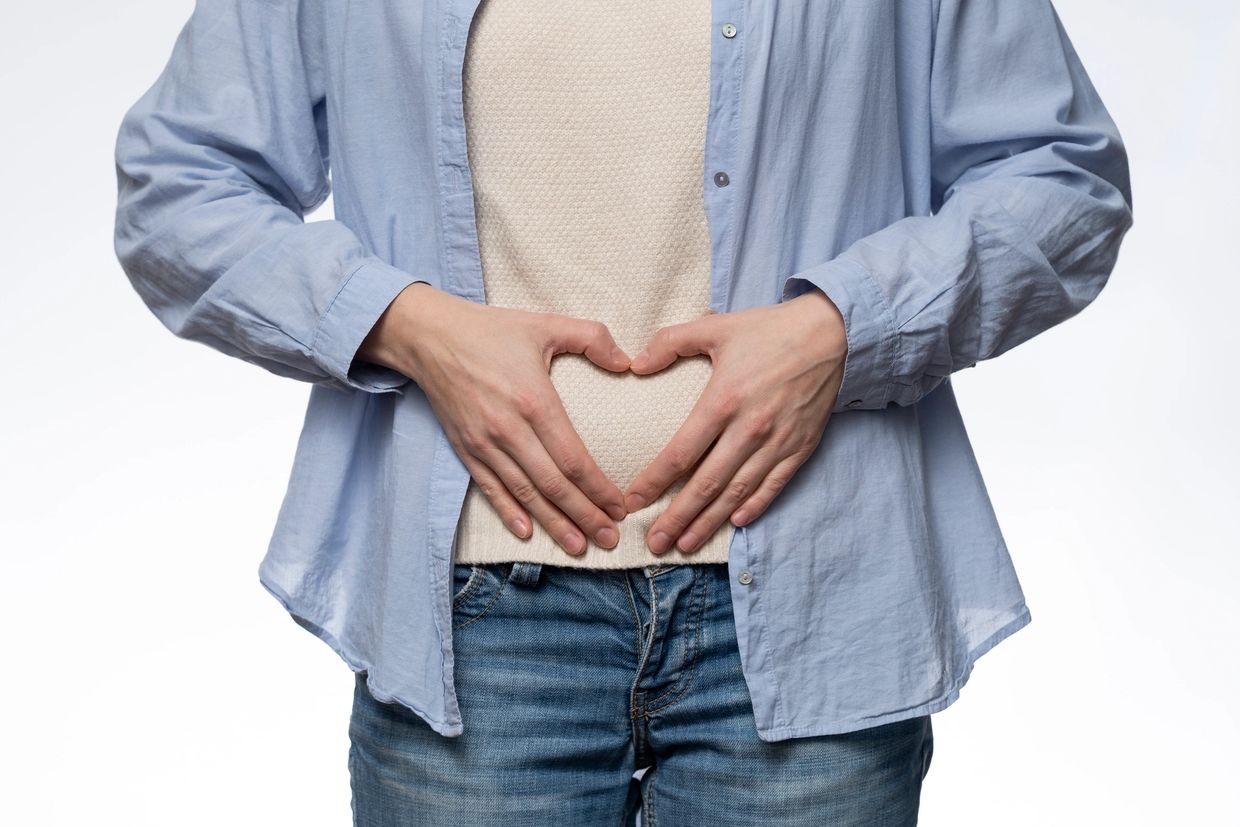 Person forming a heart with hands over stomach.